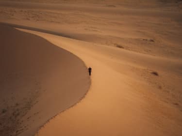 Zoom out shot of man walking on sand dune